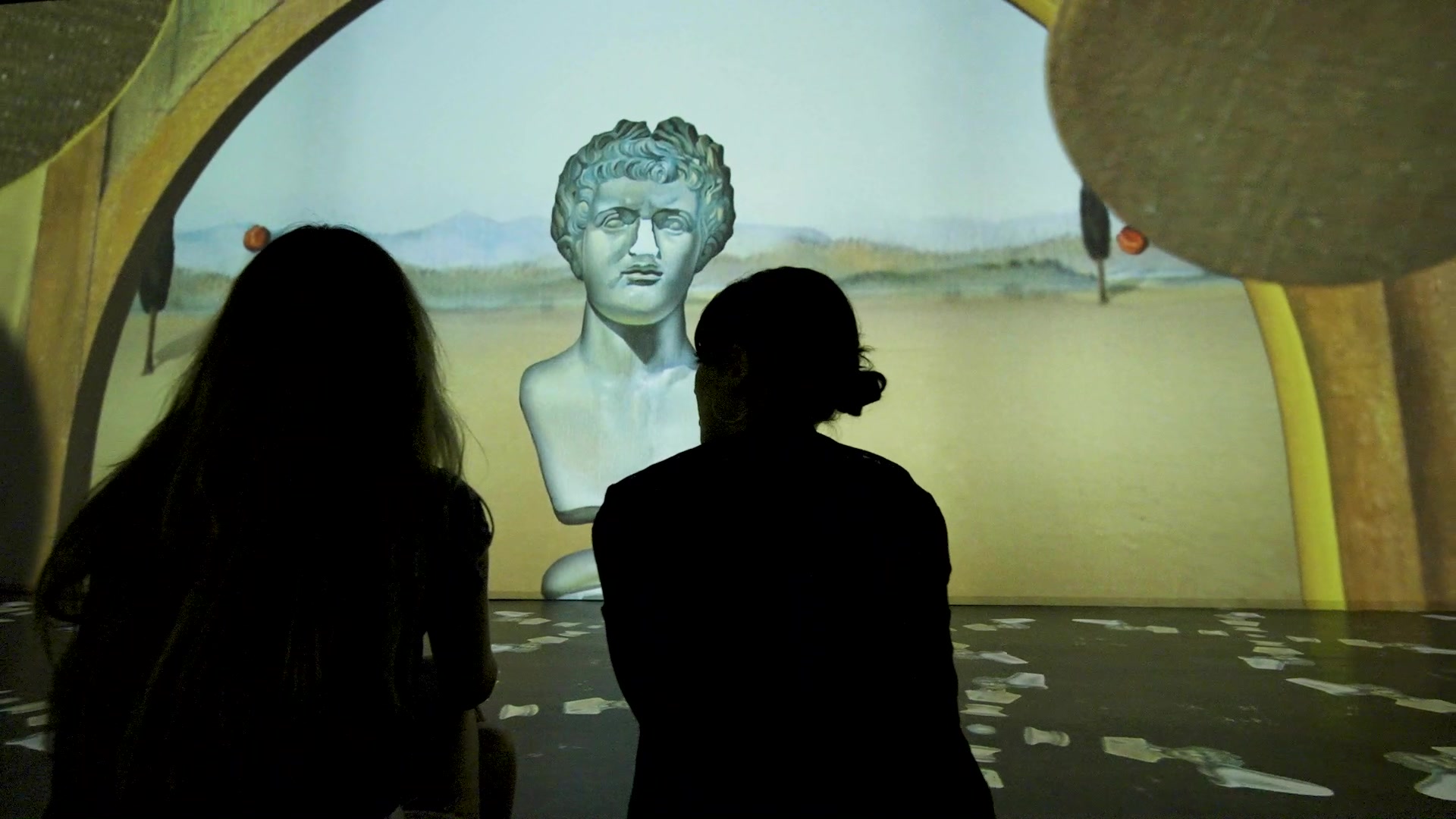 Dalí Cybernetics sergisinde Dalí'nin gerçeküstü manzaralarının projeksiyonu önünde ziyaretçiler