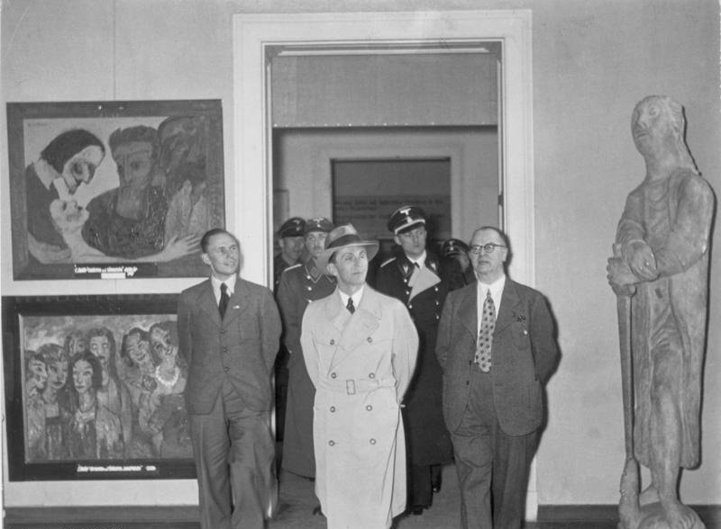 Siyah beyaz fotoğraf: Goebbels ve yanındakiler, duvarda Emil Nolde resimleri asılı Yozlaşmış Sanat sergisinde yürüyor