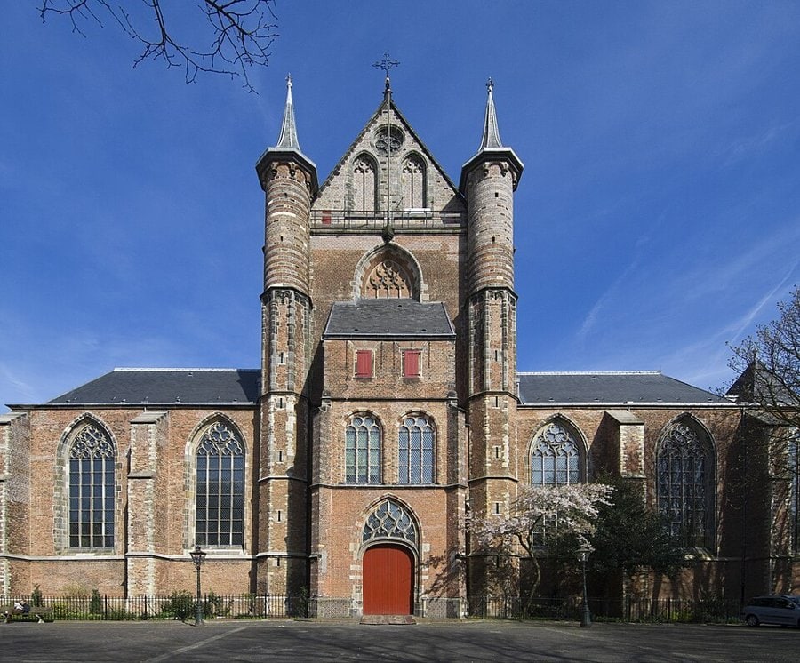 Leiden'deki Pieterskerk'in iki kuleli tuğla gotik cephesi, kırmızı kapısı ve önündeki meydan, mavi gökyüzü