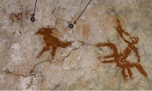 Muna Adası'ndaki mağara duvarında kızıl kahverengi hayvan figürleri ve altlarında seçilen solgun el şablonu izleri