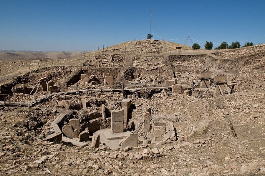 Göbeklitepe kazı alanında taş duvarlar arasında yükselen T biçimli dikilitaşlar, mavi gökyüzü altında