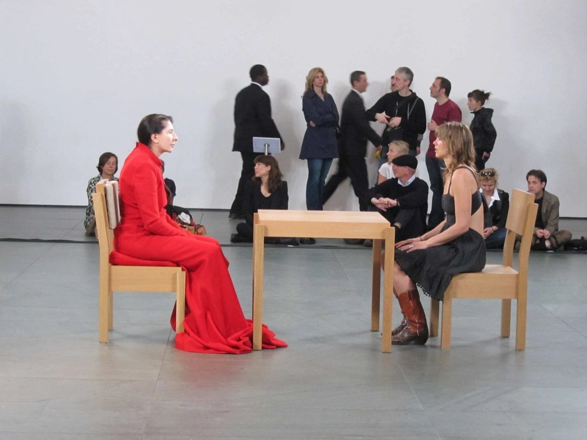 The Artist Is Present, Marina Abramović: kırmızı elbiseli sanatçı bir ziyaretçiyle masada karşı karşıya