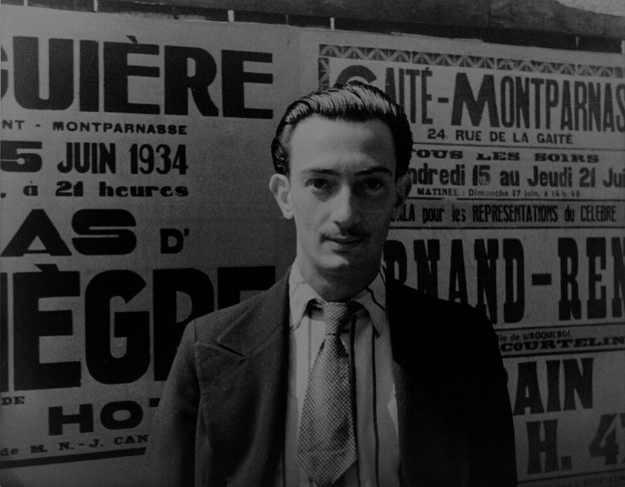 Genç Salvador Dali, Paris'te tiyatro afişleriyle kaplı bir duvarın önünde takım elbiseyle duruyor